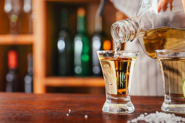 Barkeeper pouring tasty tequila from bottle into glass on counter