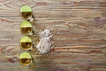 Shots of tasty tequila with lime and salt on wooden table