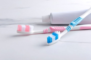 Concept of good tools for keeping teeth healthy. Closeup of plastic toothbrushes and tube of toothpaste on the white surface