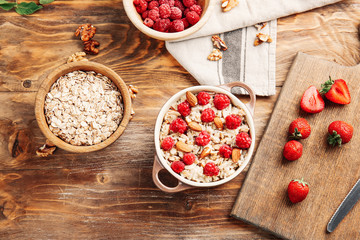 Pot with tasty sweet oatmeal, berries and almond on wooden table