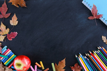 Colored pencils, notebook, crayons, red apple and fall leaves on blackboard. Top view, copy space, clack, frame, border. Education, autumn, back to school concept