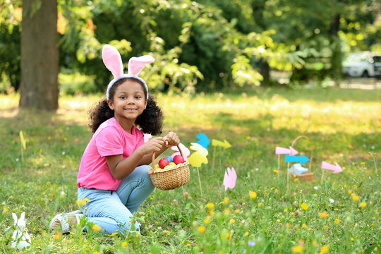 Little African-American girl gathering Easter eggs in park