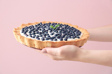 Female hands with tasty bilberry pie on color background