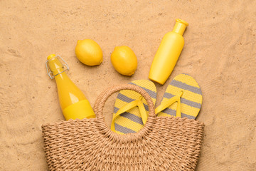 Beach bag with juice, lemons, flip-flops and cosmetics on sand
