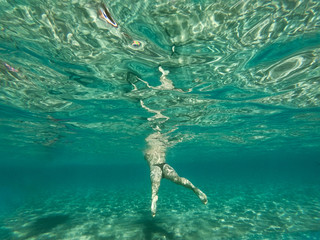 A woman swimming and walking on the sandy bottom of the sea. A girl underwater and turquoise ocean around.