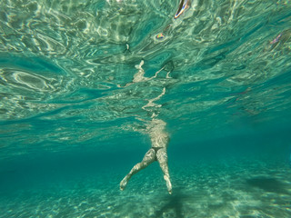 A woman swimming and walking on the sandy bottom of the sea. A girl underwater and turquoise ocean around.