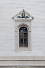 Old arched window with metall lattice and relief on a white brick wall of christian church