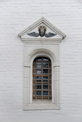 Fototapeta na wymiar Old arched window with metall lattice and relief on a white brick wall of christian church