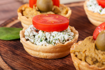 Fat paste from goose liver with tomatoes, olives and curd with greens and tomatoes on a wooden background.