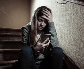 Sad depressed unhappy teenager girl suffering from cyberbullying by mobile smart phone sitting...