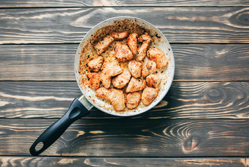 Fried chicken breast in oil and spices. Unhealthy food. Burnt pan. Damaged kitchenware.