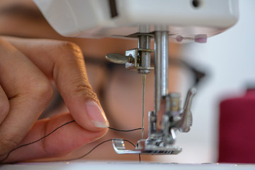 Closeup of hand of sewer or Housewife try to lead thread insert to the pin or needle of the sewing machine, old age eye of woman difficult in small tailoring works