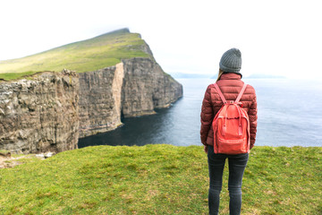 Cliffs of Vagar island and female traveller looking at outstanding Faroese nature.  Vagar, Faroe Islands.