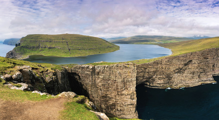 Most beautiful landmark of Vagar island - Leitisvatn lake. Amazing panorama with lake above the ocean and cliffs. Faroe Islands.
