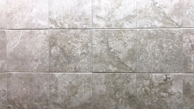 Square tiles inside bathroom on wall or floor. Color of the tiles gray and white linear design