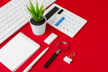 Red office desk table with blank notebook, keyboard and supplies. Top view with copy space. Flat lay.