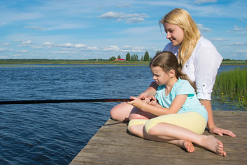 Fototapeta na wymiar mom and daughter on the pier, against the backdrop of a beautiful landscape, hold a fishing pole to catch fish, close-up, there is a place for an inscription