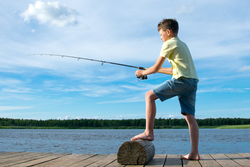 the boy on the pier, on a background of blue sky and lake, catches a fish on a bait