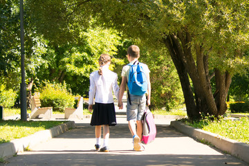 in the park, in the fresh air, schoolchildren hold hands, the rear view, the boy carries a backpack girls