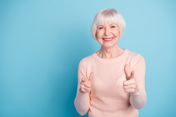 Portrait of funky granny pointing smiling wearing pink pastel sweater isolated over blue background