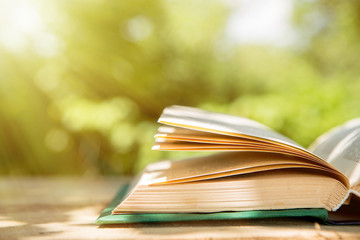 Open book on a wooden table in a garden. Sunny summer day, reading in a vacation concept