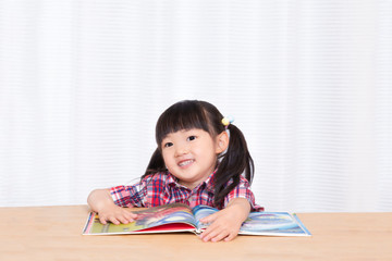 白背景の前で笑顔で絵本を読む幼い女の子。幼児、教育、読書、学習、成長、育児イメージ