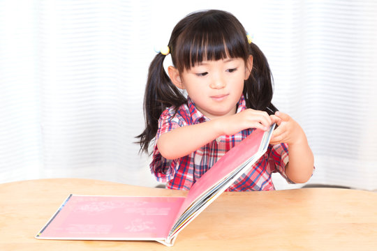 白背景の前で笑顔で絵本を読む幼い女の子。幼児、教育、読書、学習、成長、育児イメージ