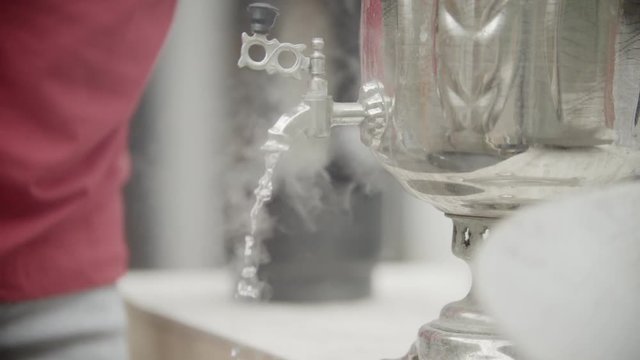 Boiling water running down from a large metal samovar with a male silhouette on the backround