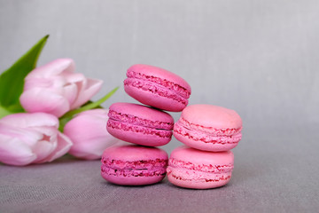 Pink and purple french macarons on grey background with flowers. Sweet food, confectionery. Space for text
