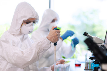 Scientists in protection suits and masks working in research lab using laboratory equipment:...