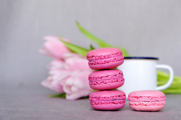 Obraz na płótnie Canvas Stack of delicious colorful macaron cookies, cup of tea or coffee and spring flowers on neutral background. Space for text