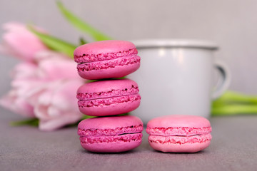 Stack of delicious colorful macaron cookies, cup of tea or coffee and spring flowers on neutral background. Space for text