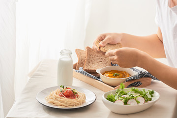 Cropped shot of male having breakfast with salad, pumpkin puree, spaghetti and milk at table in kitchen at home