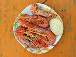 Plate of grilled prawns on a peeled rustic wooden table painted yellow