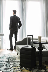 Image of successful young man standing by window in hotel apartment during business trip