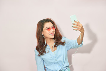 Portrait of cool cheerful girl having video-call with lover holding smart phone in hand shooting selfie on front camera isolated on light background enjoying weekend vacation