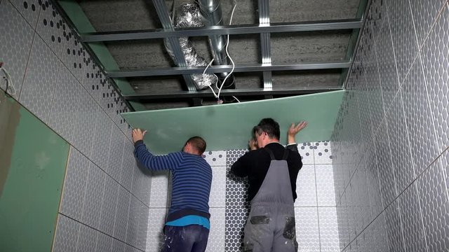 Workers men hang gypsum plasterboard sheet on ceiling
