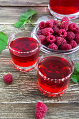 Raspberry liqueur in glass, fresh natural ripe organic berries and green leaves on a rustic wood background. Alcoholic flavored drink.