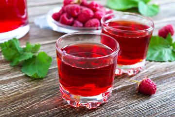 Raspberry liqueur in glass, fresh natural ripe organic berries and green leaves on a rustic wood background. Alcoholic flavored drink.