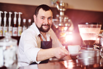 portrait of a handsome bearded barista preparing coffee on the background of a coffee shop and a coffee machine