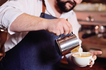 barista or coffee barman prepares coffee with a pattern on the foam or latte-art