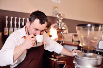 cute bearded barist man with a cup of coffee or demitasse in his hands on the background of a cozy coffee house