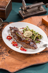 Grilled Flank Steak with green beans on white plate on old map background