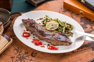Grilled Flank Steak with green beans on white plate on old map background