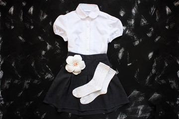School uniform with white shirt, socks and dark denim skirt on a black background. Flatlay, top view, copy space.