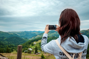 A young girl tourist with a backpack standing on top of a mountain photographs on a telephone a mountain landscape. The concept of active holidays, travel, holidays in the mountains