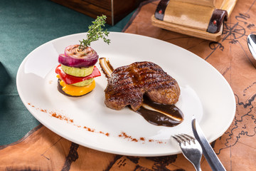 Grilled beef steak with grilled vegetables on white plate on old map background