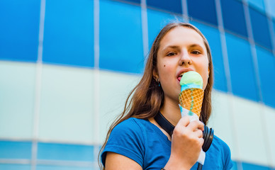 Outdoor portrait of young teenager brunette girl with long hair eating ice cream. Glass building on background with copy space