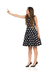 Beautiful Young Woman In Black Cocktail Dress In Polka Dots And High Heels Is Touching Something