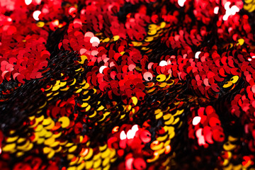 Background of sequin. Fashion shiny fabric. Scales of round sequins. Festive abstract glittery background. Red and golden two-sided sequins. Selective focus. 